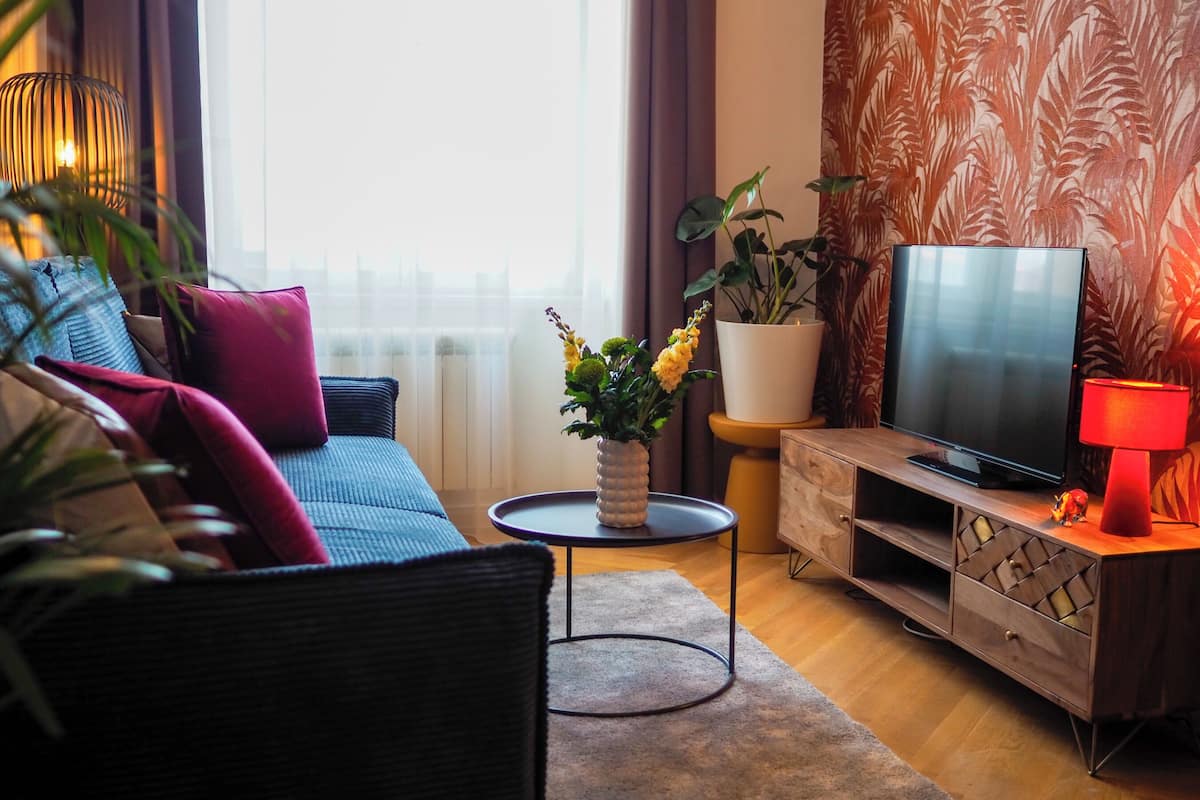 A modern living room with a sofa, a round coffee table, a TV stand, and a potted plant.
