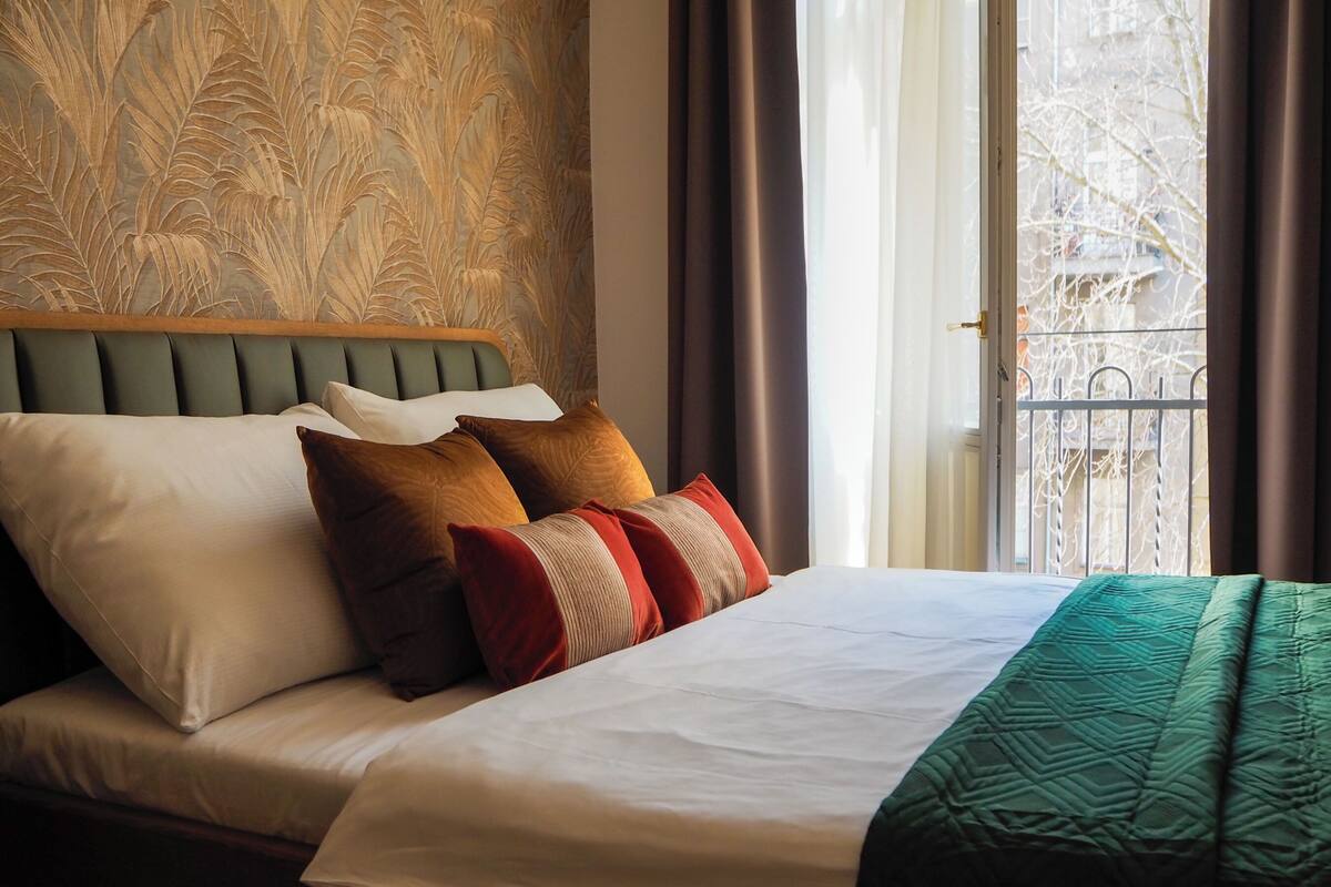 A neatly made bed with a green headboard, white and brown pillows, and a green blanket.