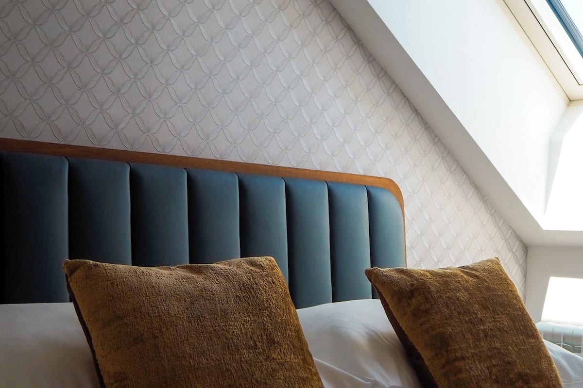 A bedroom with a sloped ceiling, a tufted headboard, and two brown pillows.