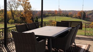 A covered patio with a table and chairs, offering a view of a grassy landscape and trees.
