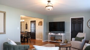 A living room with a television, two sofas, a coffee table, and a dining area in the background.