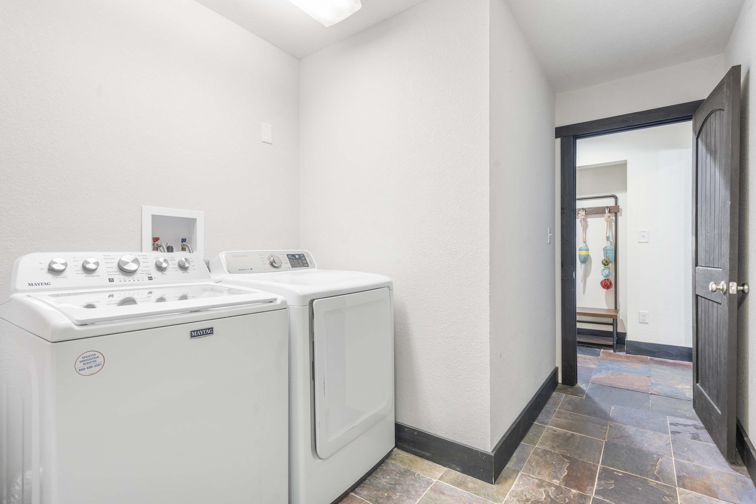 A laundry area with a Maytag washer and dryer, a small white shelf with toiletries, and a tiled floor.