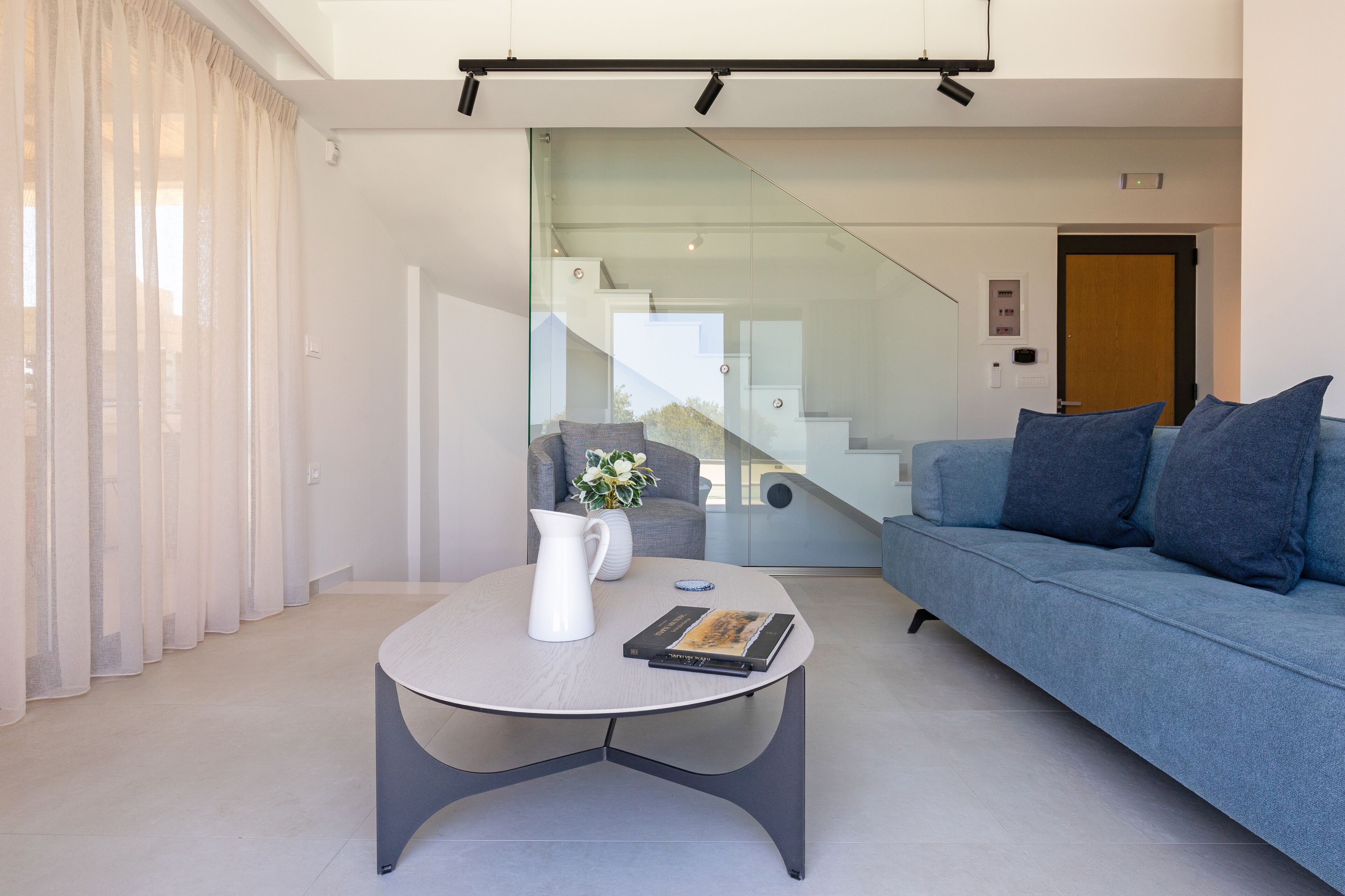 Ein modernes Wohnzimmer mit einem grauen Sofa, einem weißen Couchtisch und einer Glasstufenanlage, die zu einer weiteren Ebene führt.