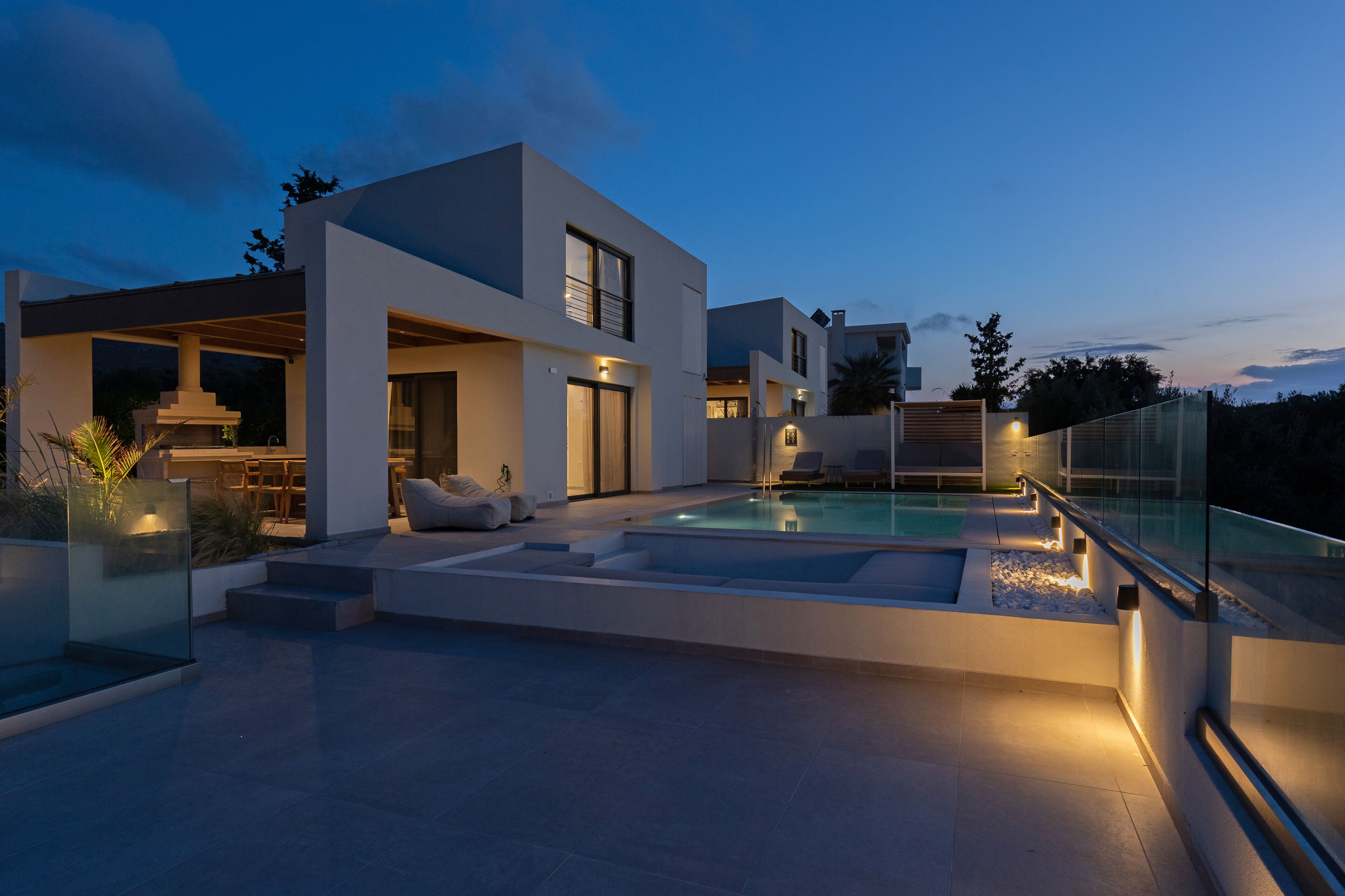 Una casa moderna con piscina, mobiliario exterior y barandilla de cristal.