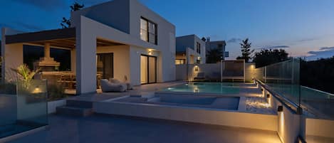 Una casa moderna con piscina, mobiliario exterior y barandilla de cristal.
