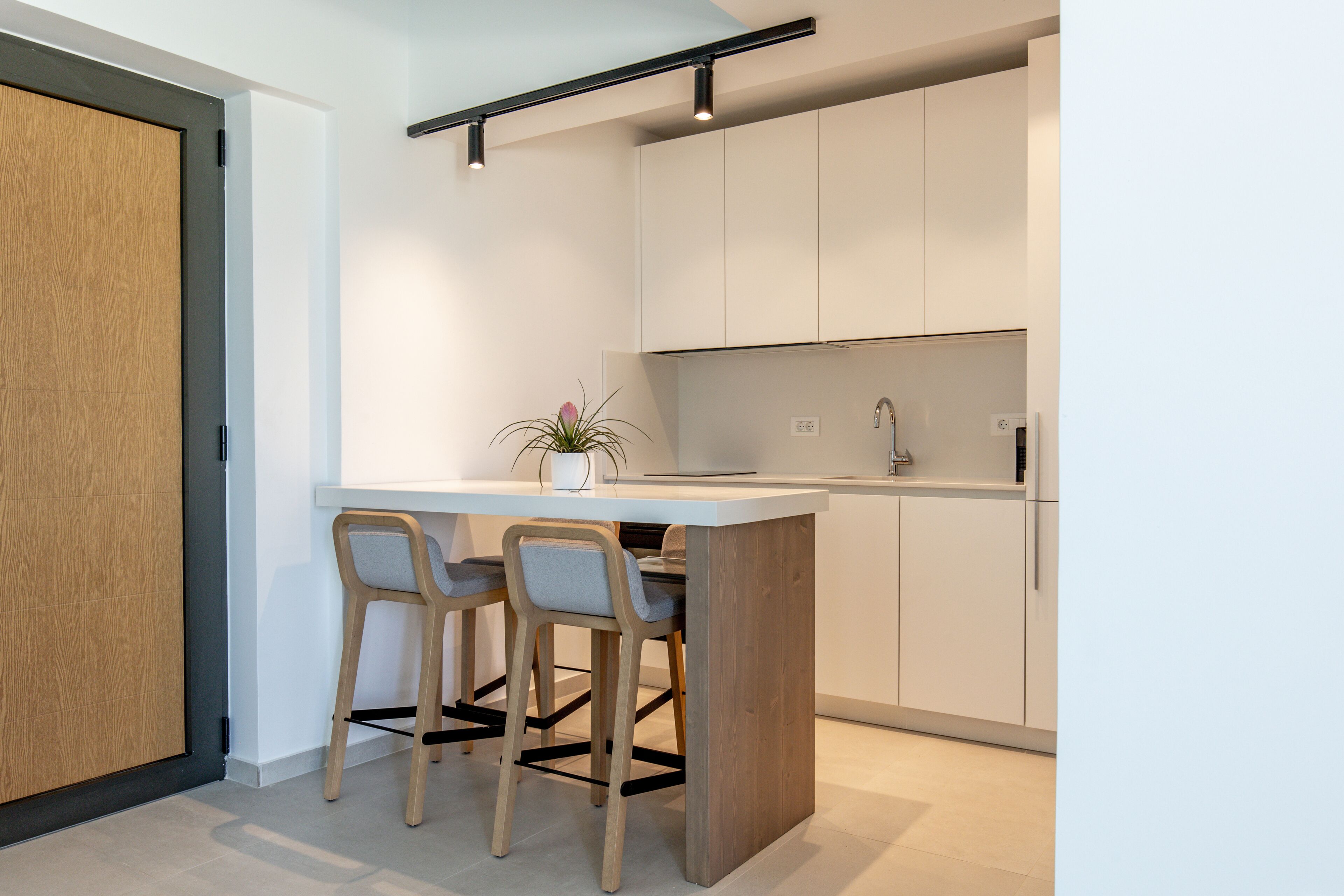 A modern kitchen with a central island, two bar stools, and a potted plant.