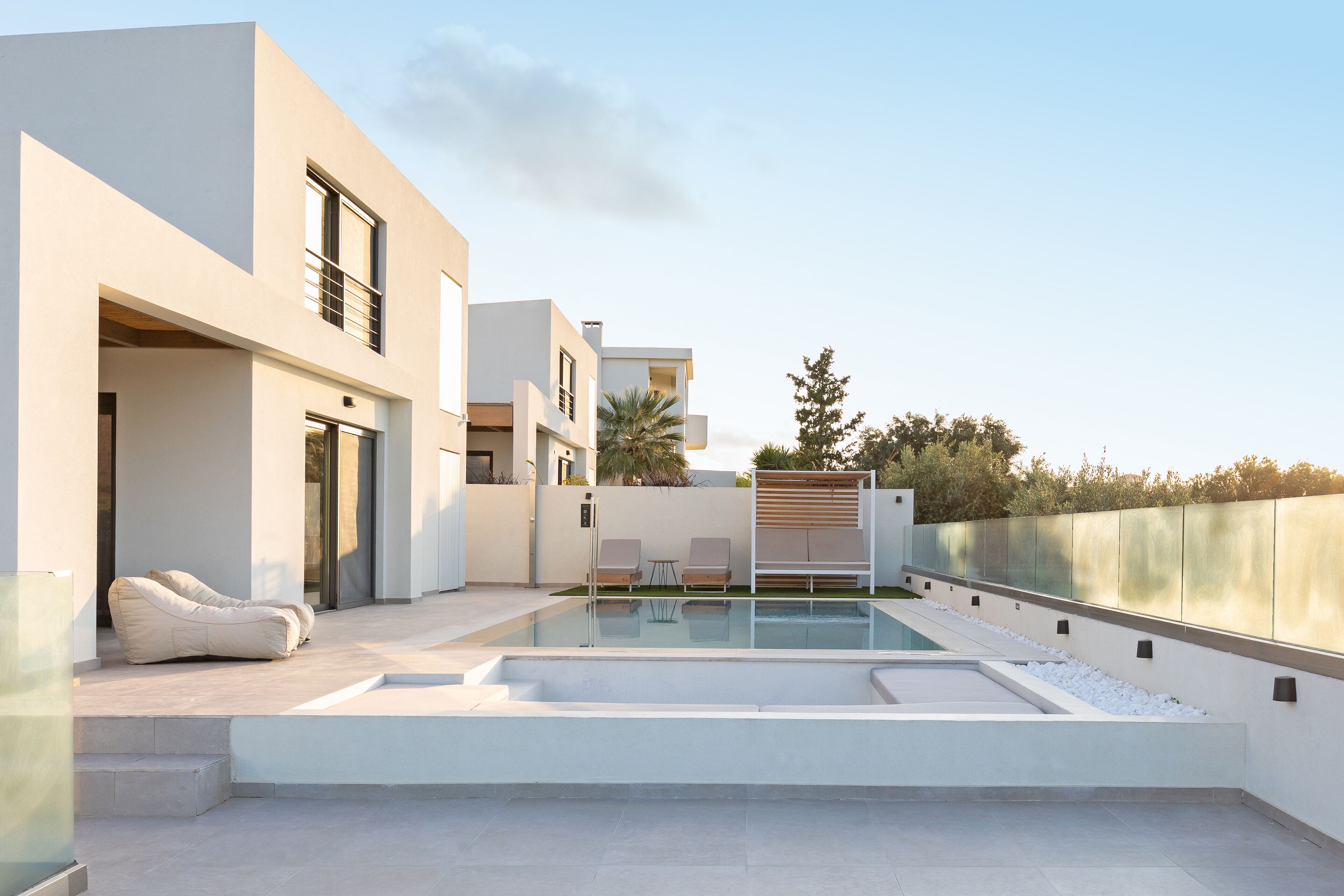 Un espace piscine extérieur moderne, doté d’un design minimaliste, comprenant un coin salon avec deux chaises et un fauteuil poire, et offrant une vue dégagée sur la piscine.