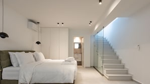 A modern bedroom with a bed, a glass staircase, and a bathroom in the background.