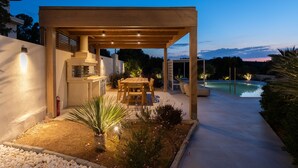 A covered outdoor dining area with a pool in the background.