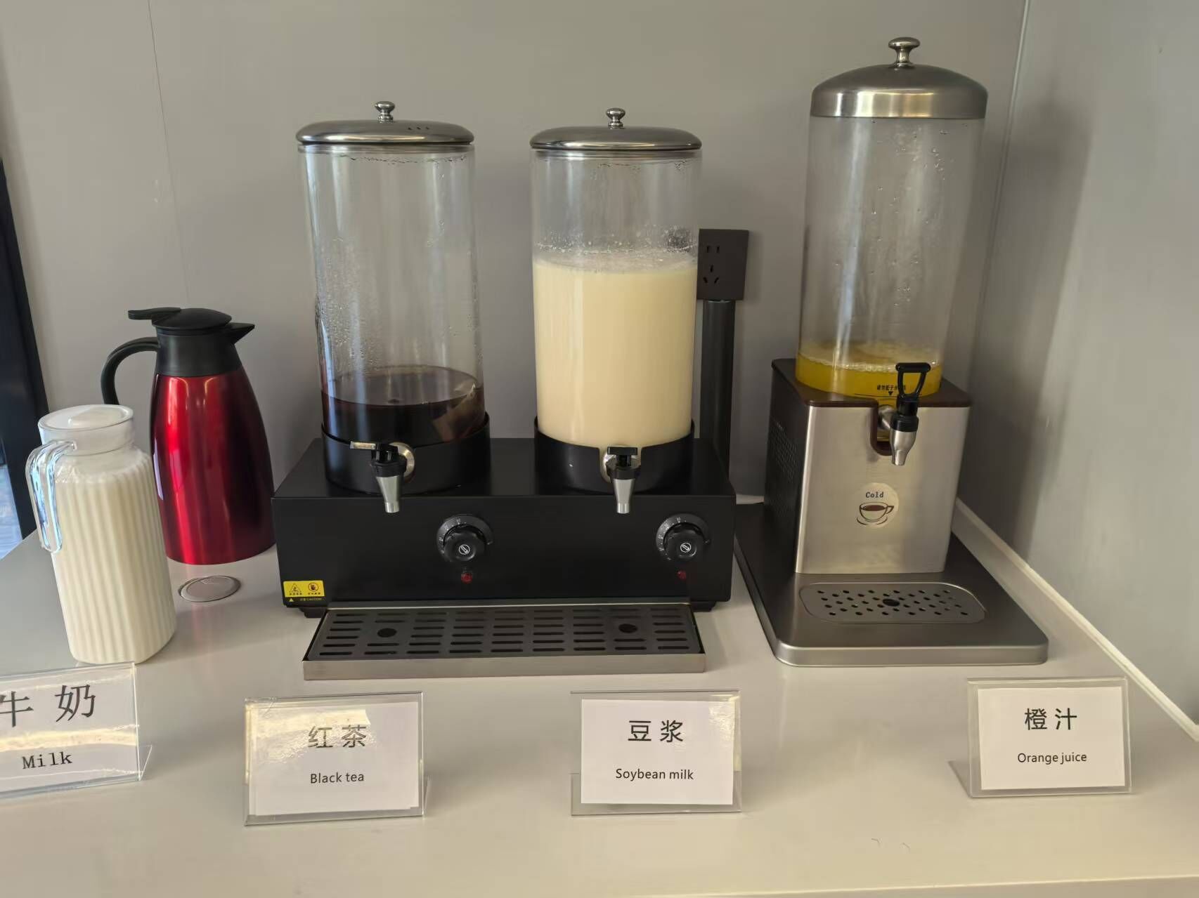 A beverage station with dispensers for milk, black tea, soybean milk, and orange juice.