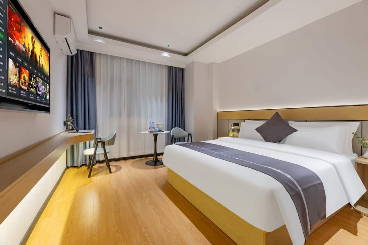 Una habitación de hotel con una cama grande, un escritorio y un televisor montado en la pared.