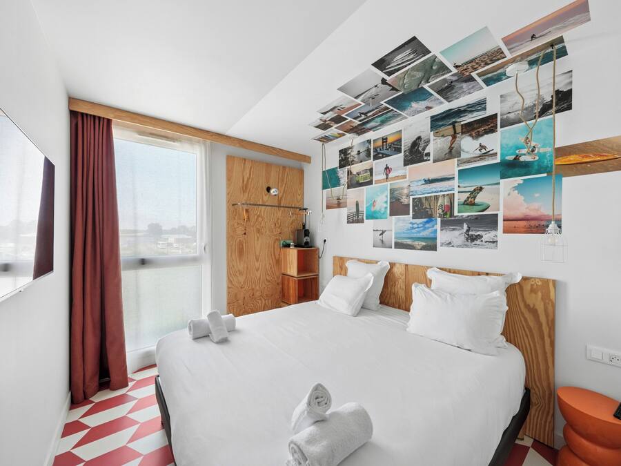 A hotel room with a large bed, a wall of photos, a window with curtains, and a view of the city.