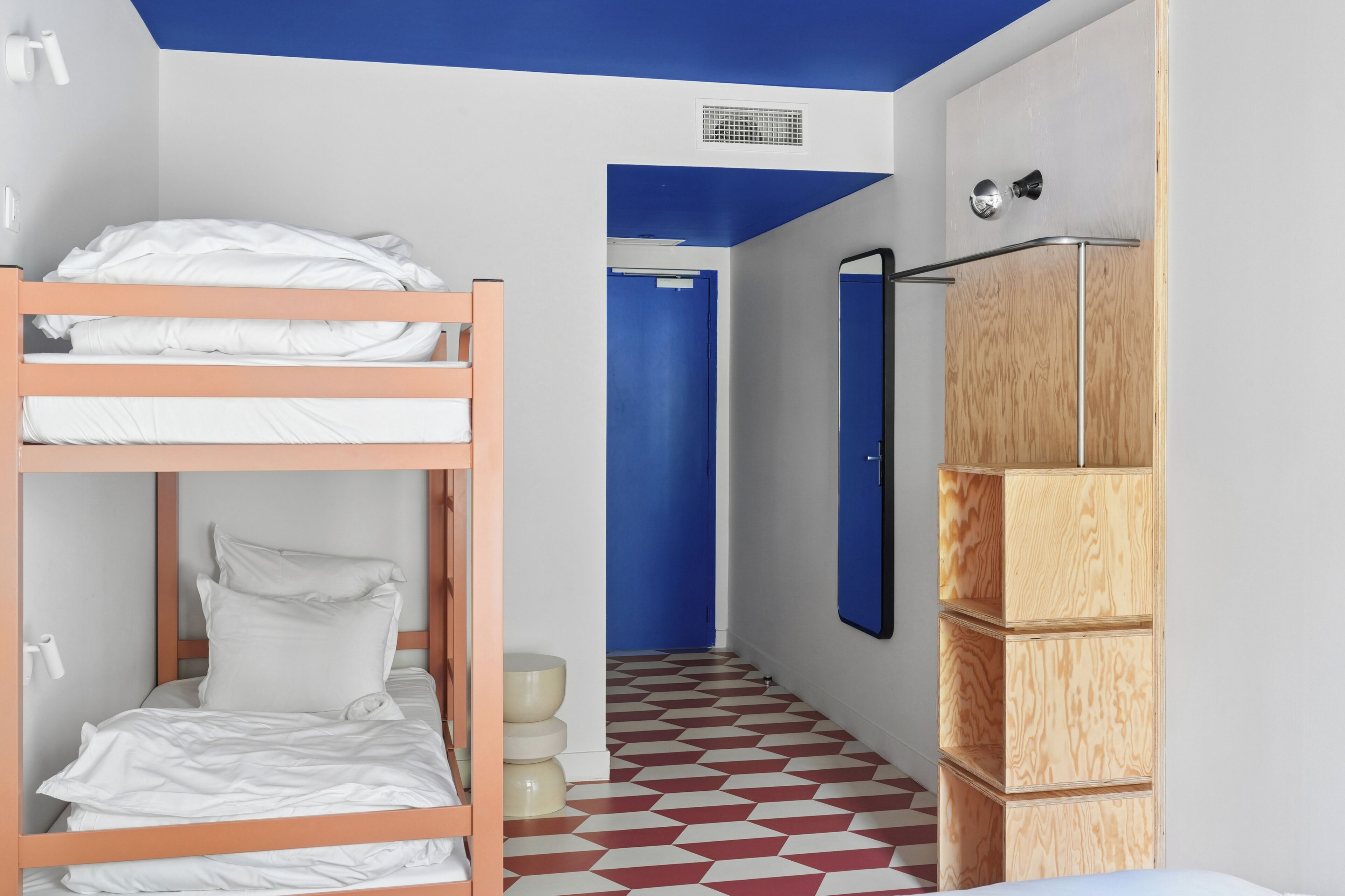 Une pièce avec des lits superposés, une porte bleue, un miroir et un sol à motifs.