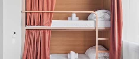 A bunk bed room with a wooden headboard, white bedding, and a red curtain.