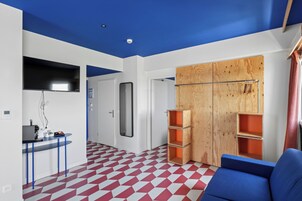 Una habitación moderna con suelo de patrón geométrico, un sofá azul, un armario de madera con estantes y un escritorio con una computadora y otros objetos.