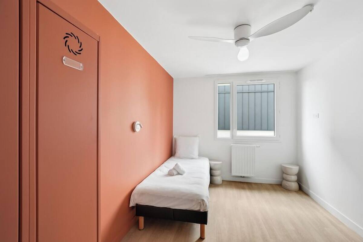 Een slaapkamer met een bed, plafondventilator, raam en radiator.