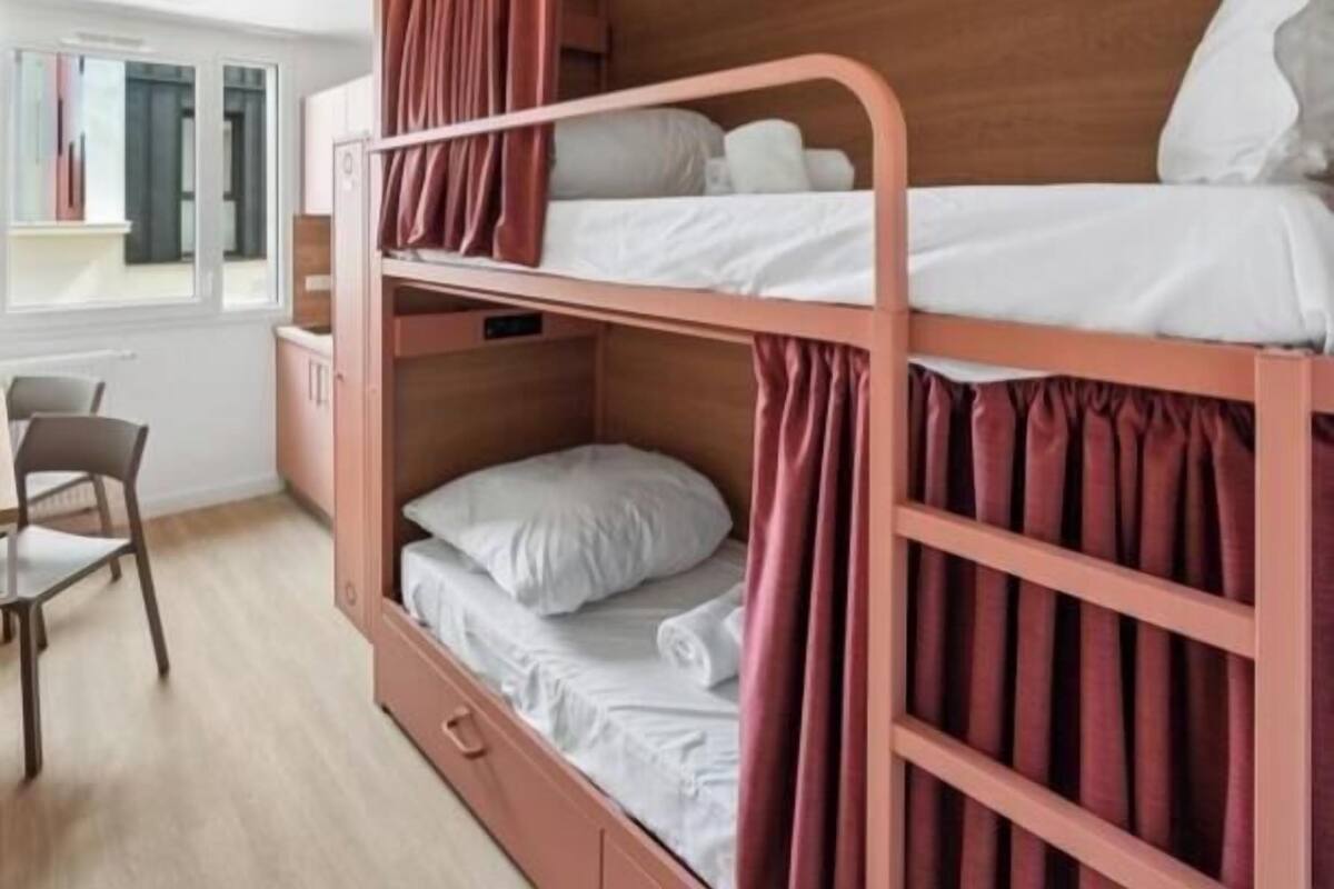 Een stapelbed met twee verhogingen, een houten hoofdbord en een bureau met stoel.