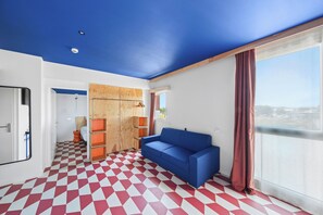 Une pièce avec un sol à carreaux, un canapé bleu, une armoire en bois et une grande fenêtre donnant sur un beau paysage.
