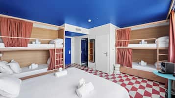 A hotel room with bunk beds, a desk, a chair, a small table, and a shower area.