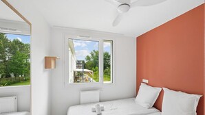 Een slaapkamer met twee bedden, een raam, een plafondventilator en uitzicht op groen.