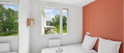 A bedroom with two beds, a window, a ceiling fan, and a view of greenery outside.