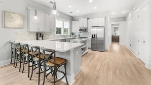 Une cuisine moderne avec des meubles blancs, un grand îlot central doté de tabourets, des appareils en acier inoxydable et un éclairage suspendu.