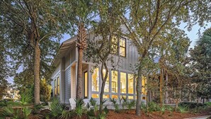 Une maison à deux étages avec de grandes fenêtres, entourée d’arbres et de plantes.