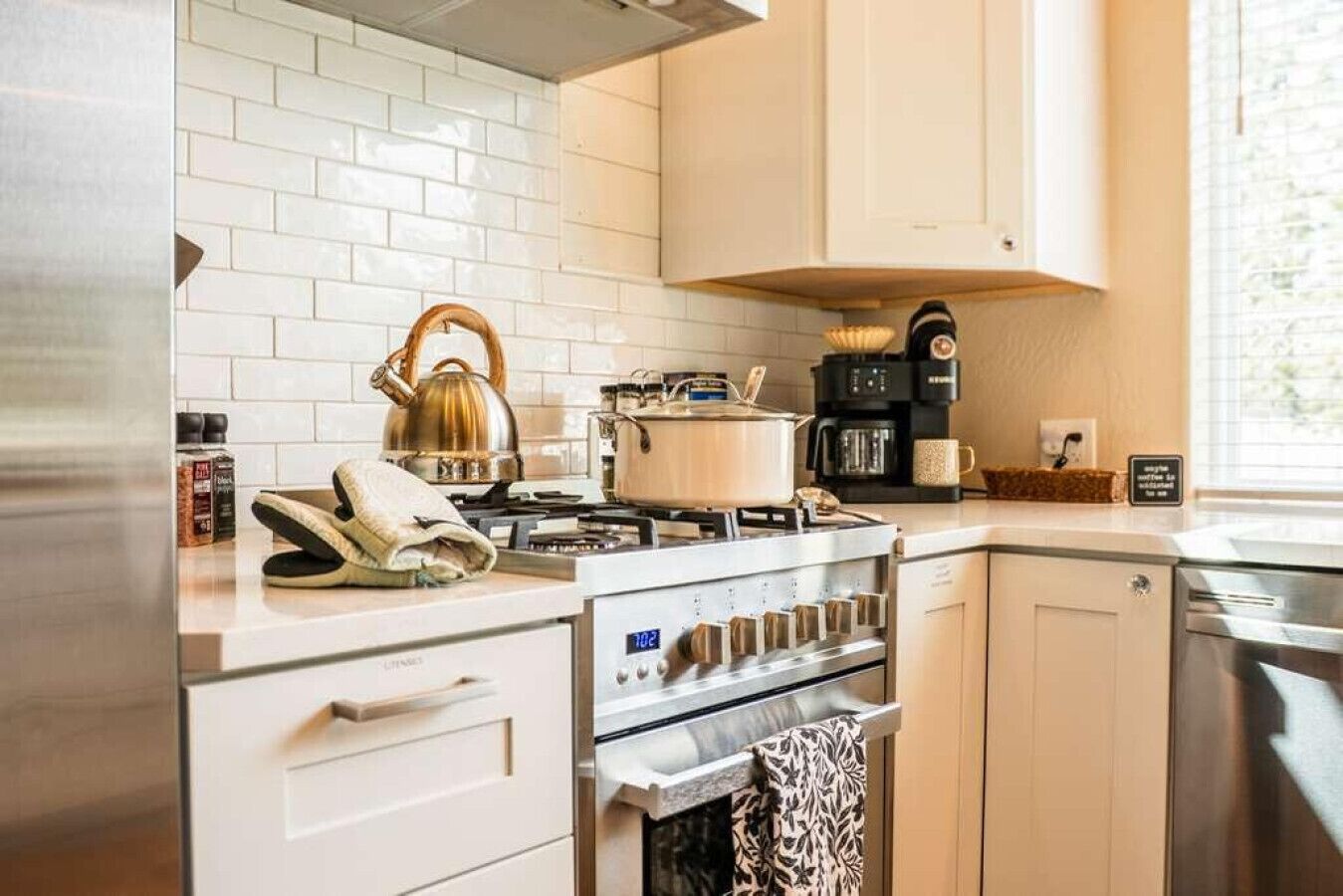 A modern kitchen with white cabinetry, a gas stove, a kettle, and a coffee maker.