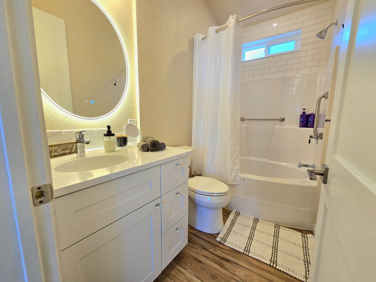 A bathroom with a white sink, toilet, and bathtub. There is a mirror with a light above it, and a shower curtain.