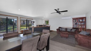 A spacious living area with a dining table, comfortable seating, a ceiling fan, and a bookshelf. - Alpine Edge Retreat - Gateway to Mount Buller (Merrijig)
