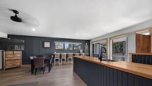 A modern kitchen with a wooden countertop, a built-in stove, and a dining area with wooden chairs and a table. - Alpine Edge Retreat - Gateway to Mount Buller (Merrijig)