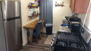 Una cocina compacta con un refrigerador de acero inoxidable, una mesa de comedor de madera con sillas azules, una estufa a gas y una pequeña encimera con un lavamanos.