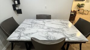 A dining area with a marble table, four upholstered chairs, a wall-mounted TV, and a decorative wall piece. - Spacious & Accessible 2-bedroom Condo with Pool & Private Garage, BEST LOCATION! (Las Vegas)