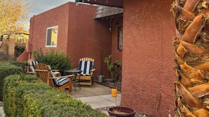 A house with a red brick exterior, a dark roof, and a small patio area with two Adirondack chairs and a table. - Spacious & Accessible 2-bedroom Condo with Pool & Private Garage, BEST LOCATION! (Las Vegas)