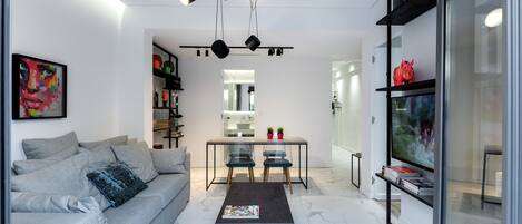 A modern living room with a grey sofa, a glass coffee table, and a dining area with a table and chairs.