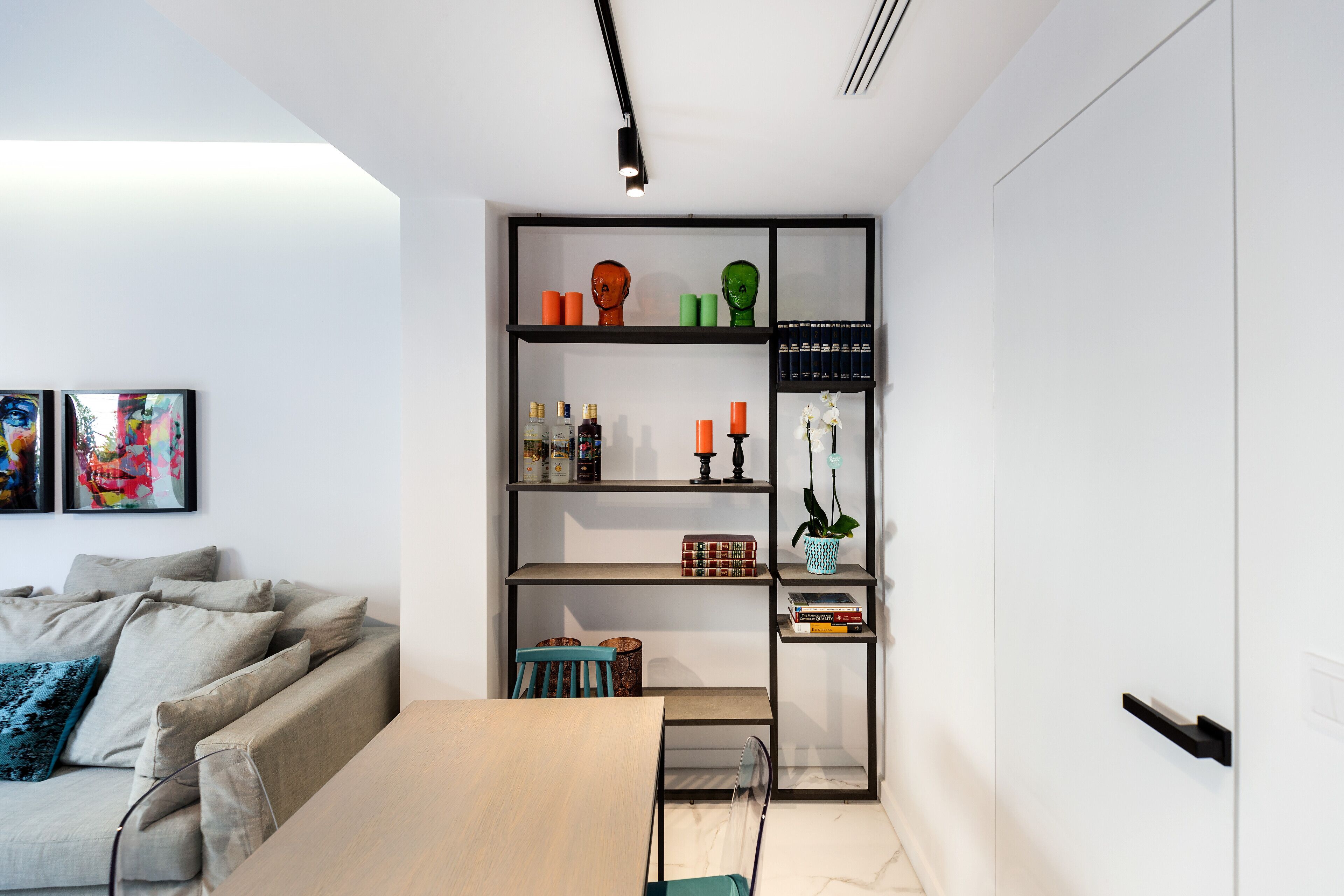 Un salon moderne avec un canapé, une table en bois et une étagère noire contenant divers objets.