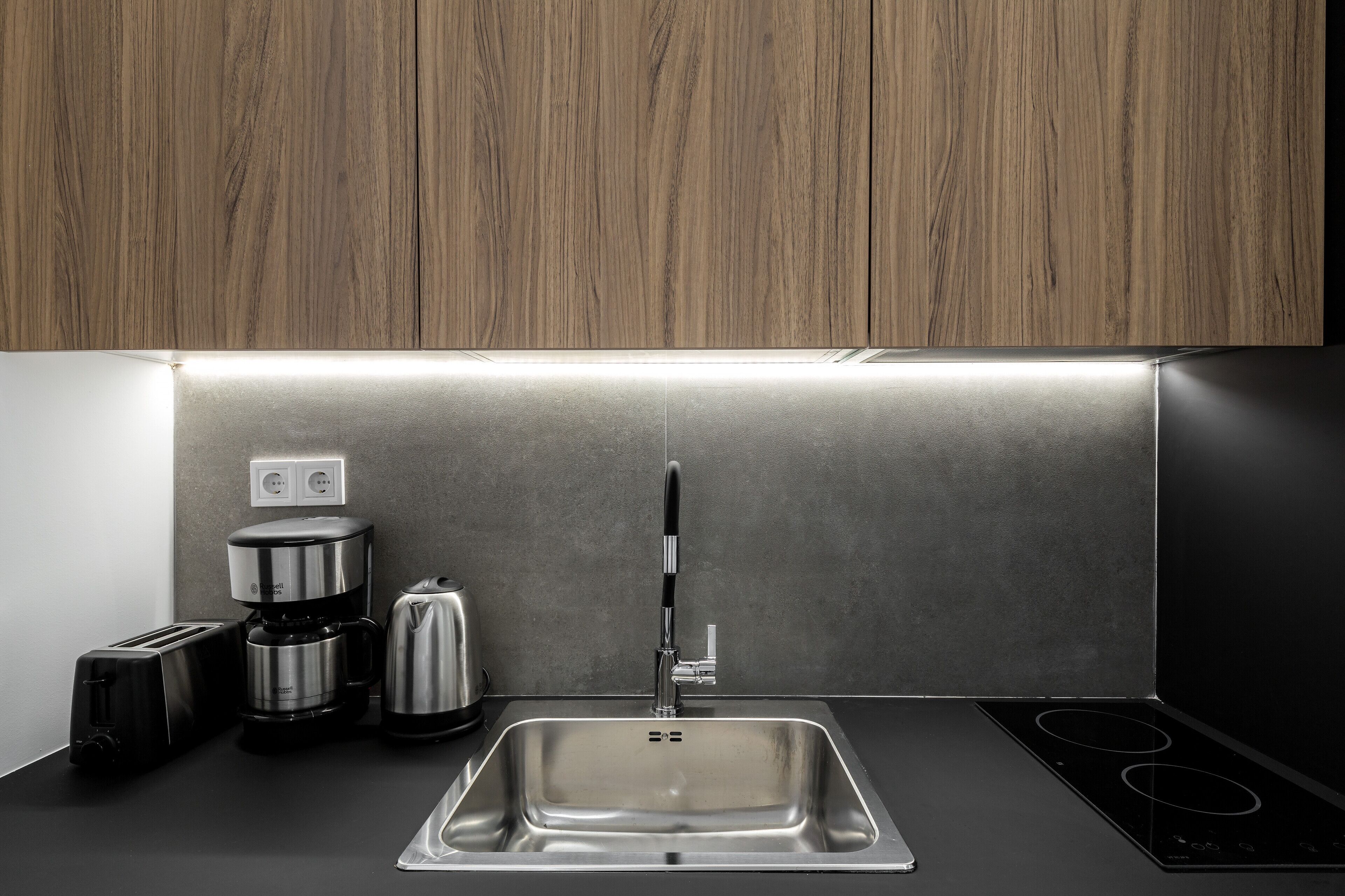 A modern kitchen with a stainless steel sink, a coffee maker, a toaster, and a kettle.