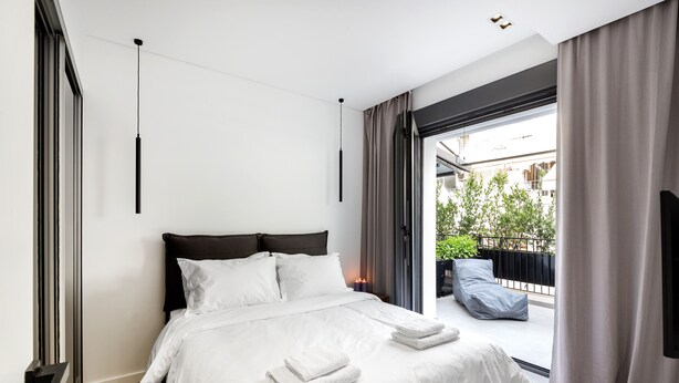 A modern hotel room with a large bed, a sliding glass door to an outdoor balcony, and a minimalist design. - Elysan Urban Stays (Athens)