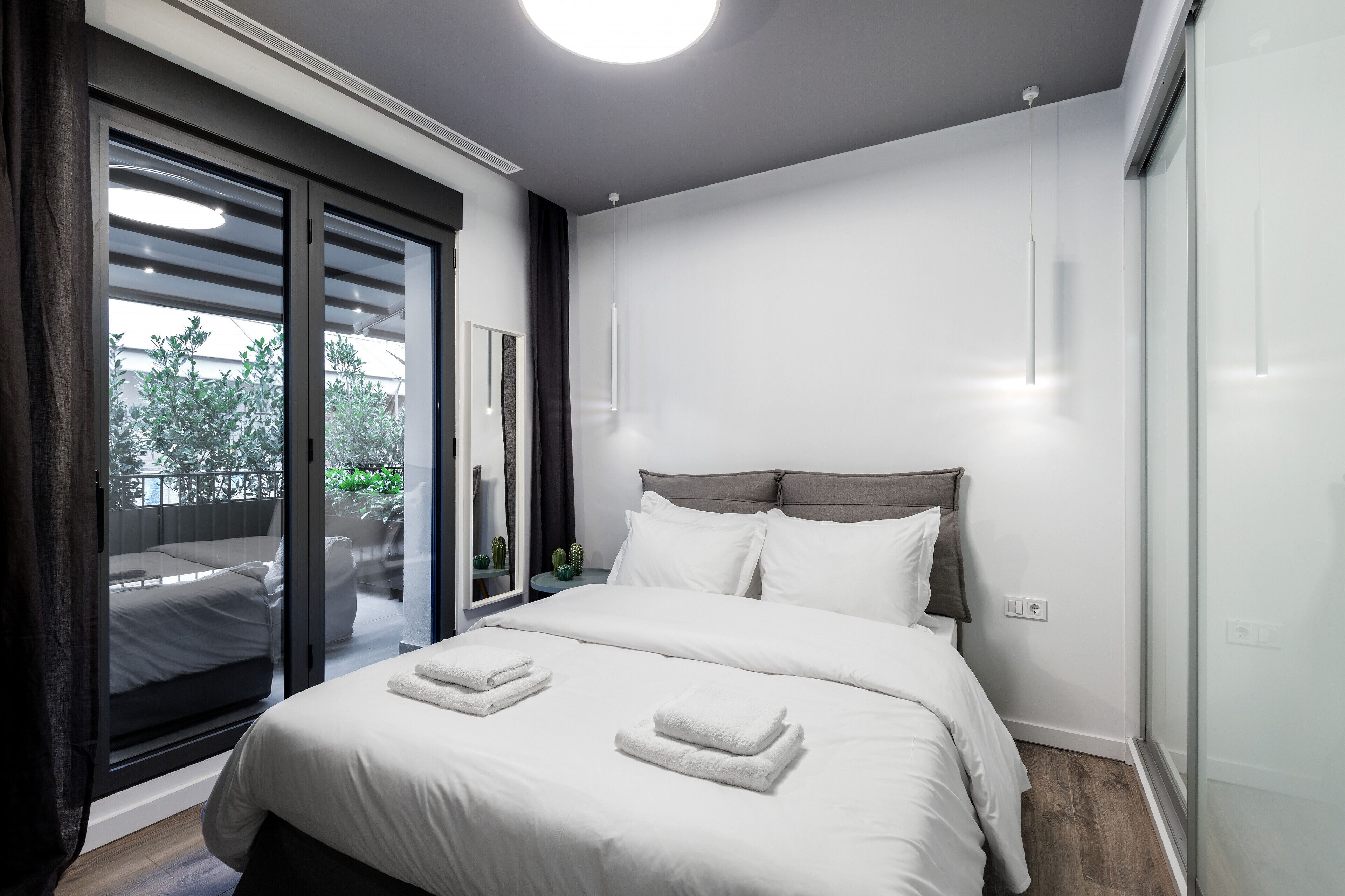 A modern bedroom with a large bed, a sliding glass door to a balcony, and a ceiling light.