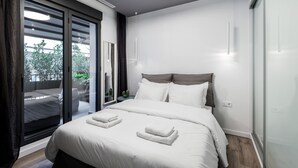 A modern bedroom with a large bed, a sliding glass door to a balcony, and a ceiling light. - Elysan Urban Stays (Athens)