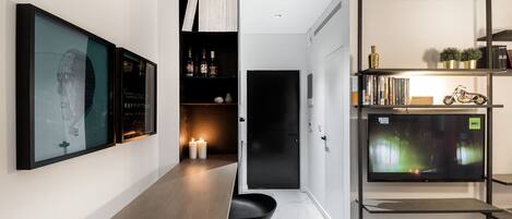 A modern interior with a long wooden table, black chairs, a TV on a shelf, and framed artwork on the wall.