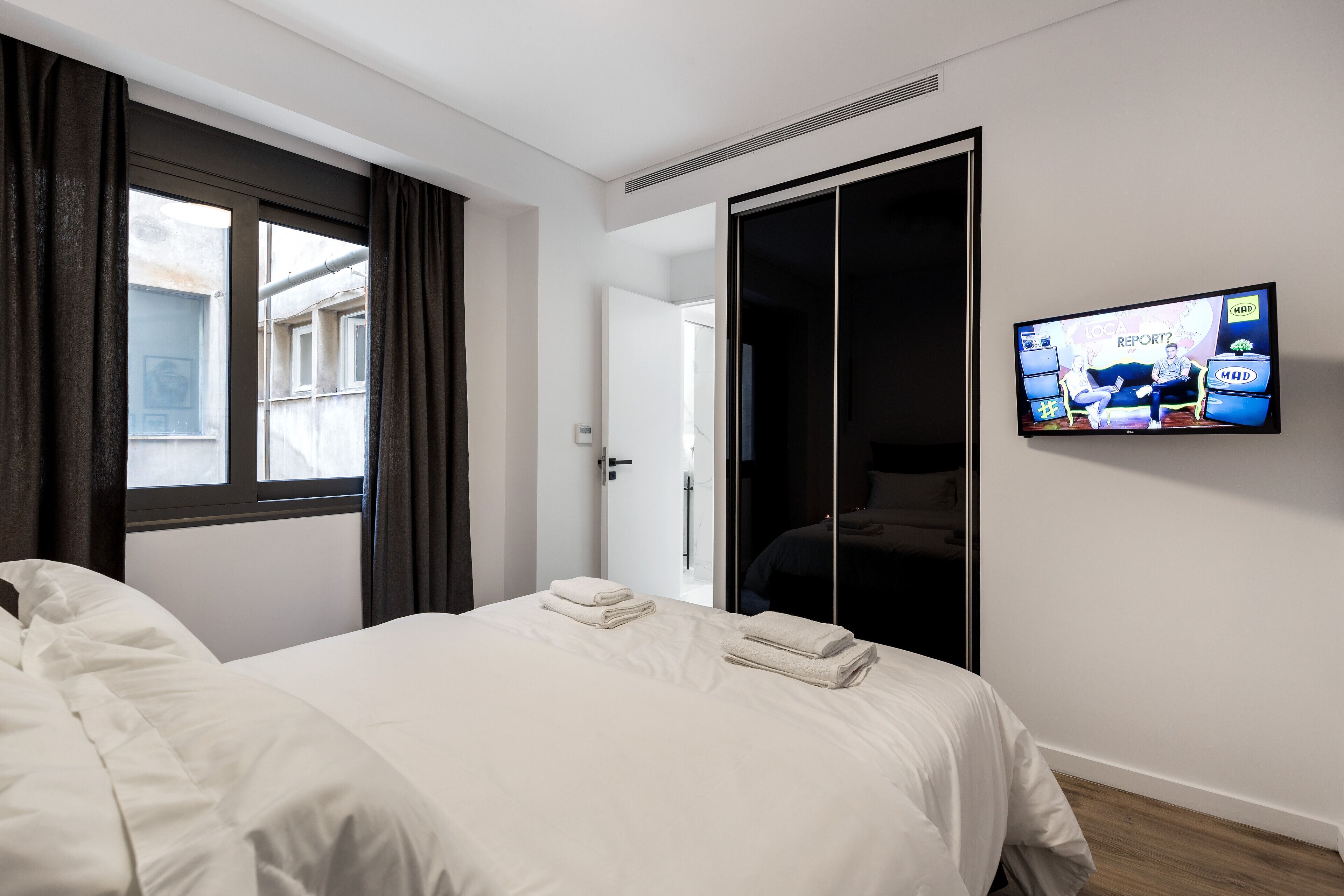 Une chambre d’hôtel avec un lit, un téléviseur fixé au mur et une fenêtre avec des rideaux.