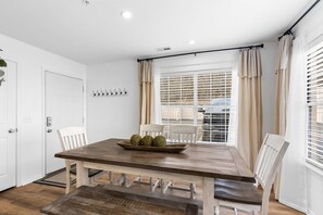 A dining area with a wooden table, white chairs, and a window with blinds.