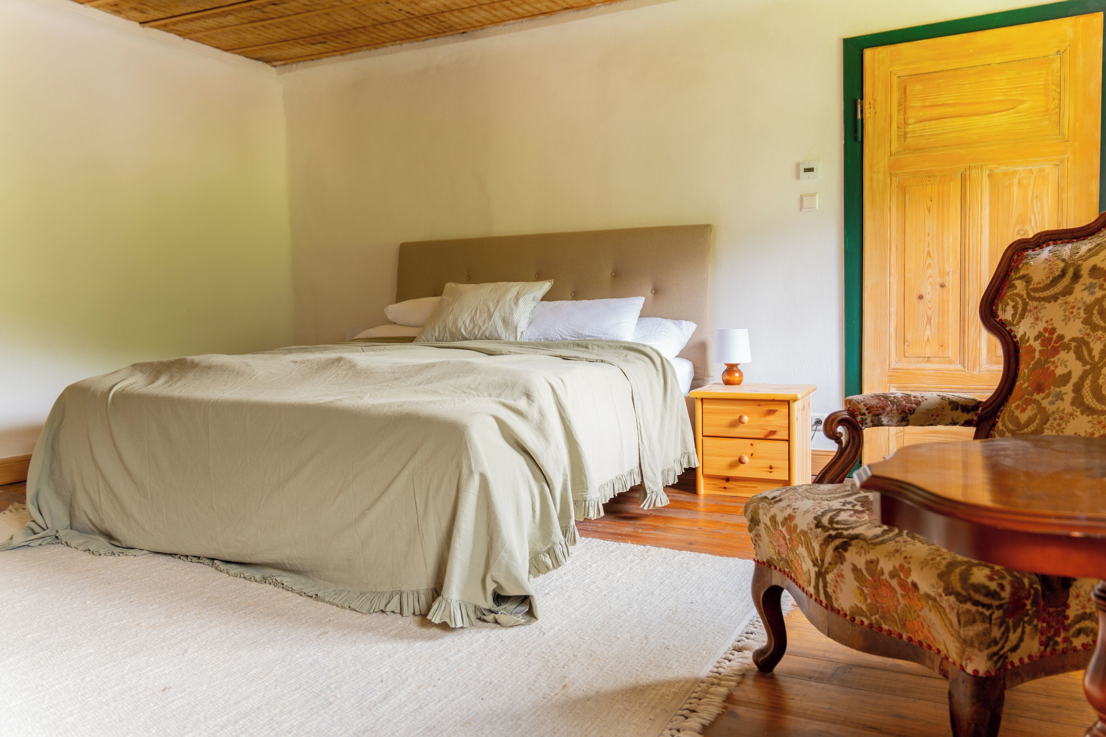A bedroom with a bed, nightstand, chair, and wooden door.