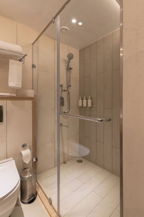 Un baño moderno con ducha de vidrio, inodoro, lavamanos y un cubo de basura.