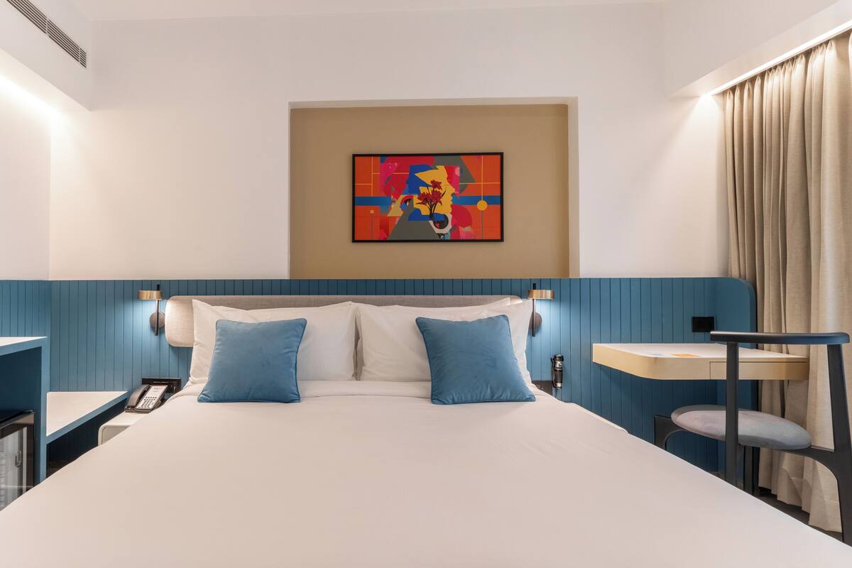 Ein Hotelzimmer mit Bett, Schreibtisch, Stuhl, Telefon und einem Bild an der Wand.