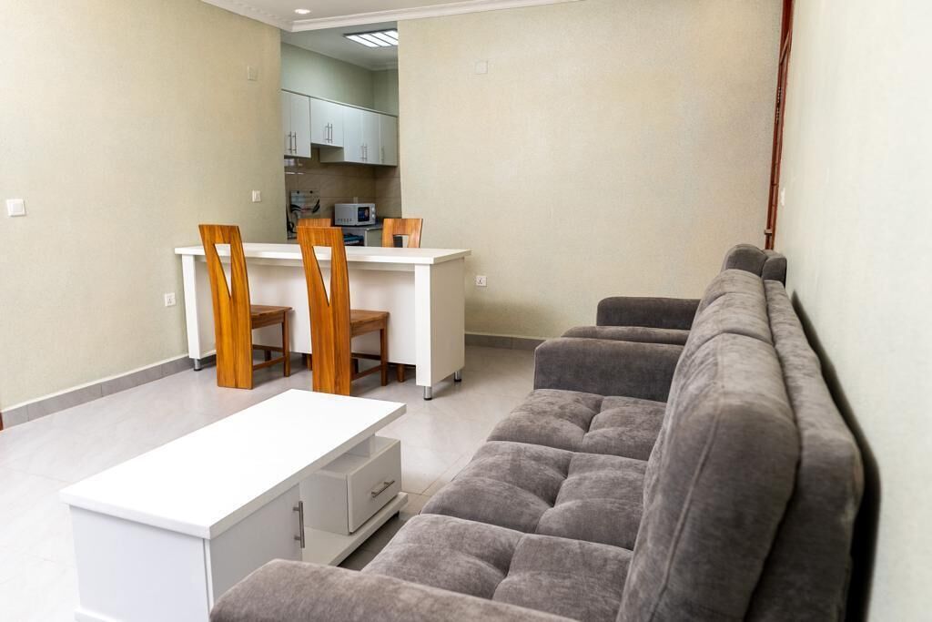 A living room with a grey sofa, a white coffee table, and a dining area with a white table and wooden chairs.