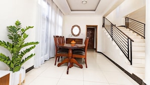 A dining area with a wooden table and chairs, a potted plant, and a staircase with black railings.