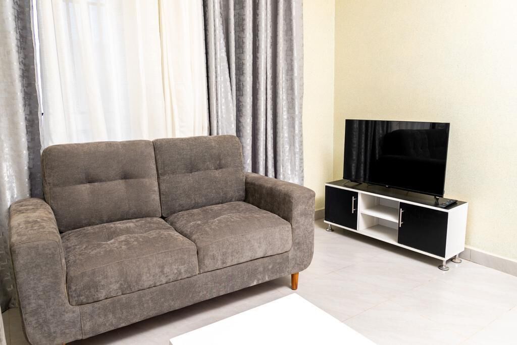Un sofá gris con un televisor sobre un mueble blanco y negro en una sala de estar.