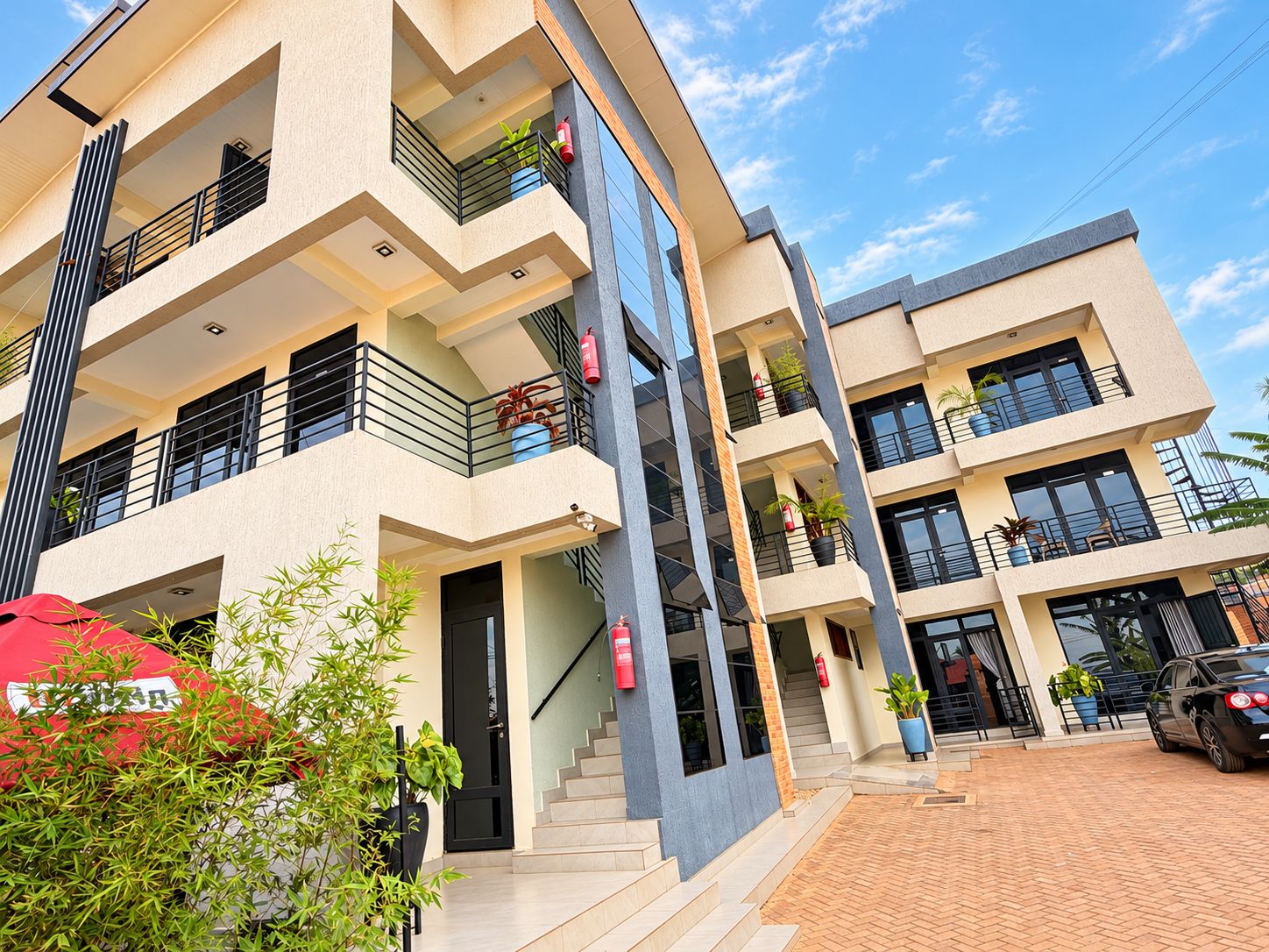 A multi-story residential building with balconies, potted plants, and a red umbrella.